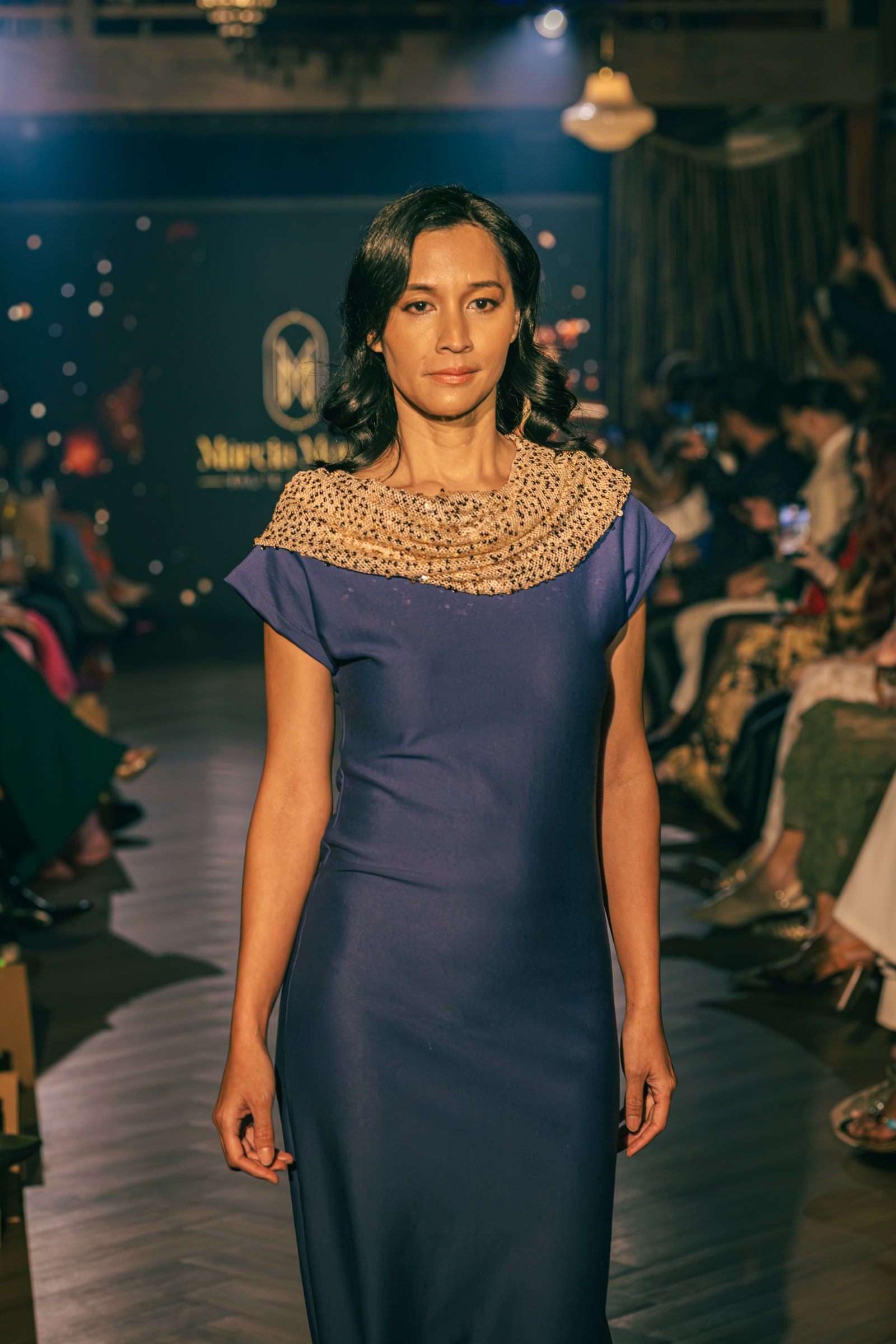 Runway model wearing a tailored navy blue dress with a textured gold neckline